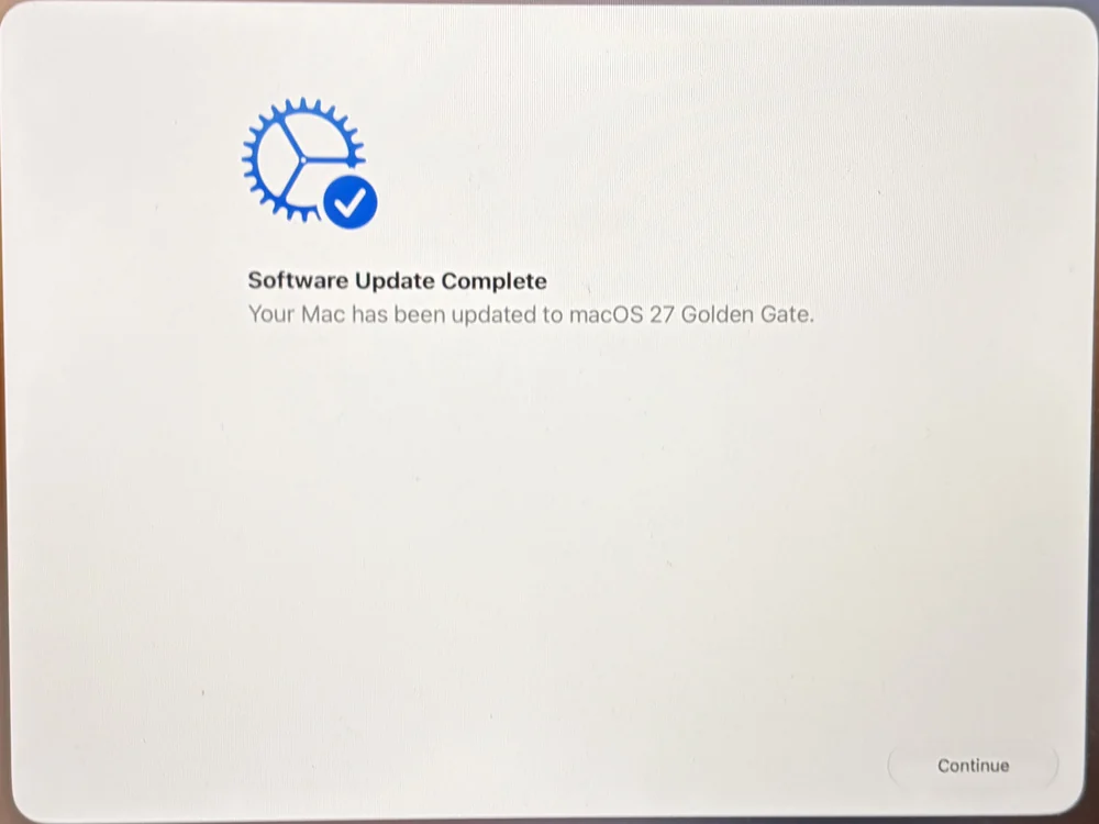 A photo of a Mac screen showing Software Update Complete, with the line Your Mac has been updated to macOS 27 Golden Gate and a Continue button